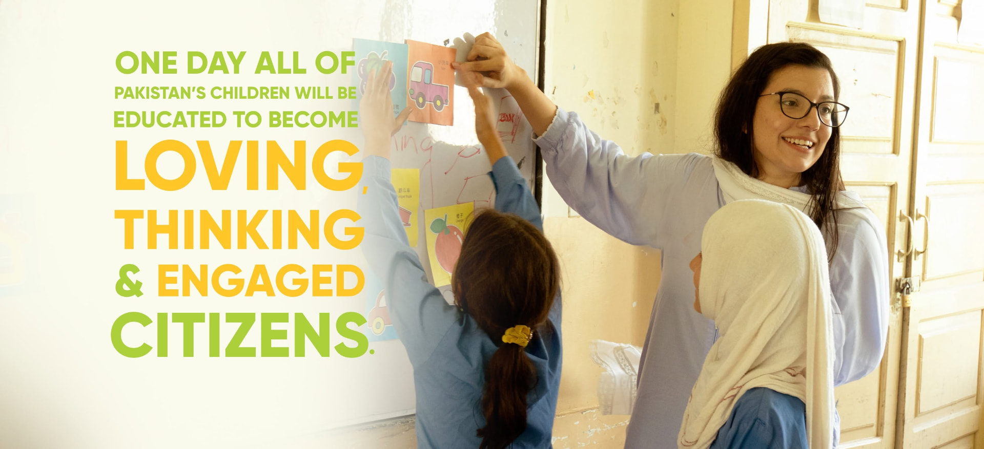 A Teach For Pakistan Fellow and her students putting up flashcards in a classroom, with the organisation's vision statement alongside