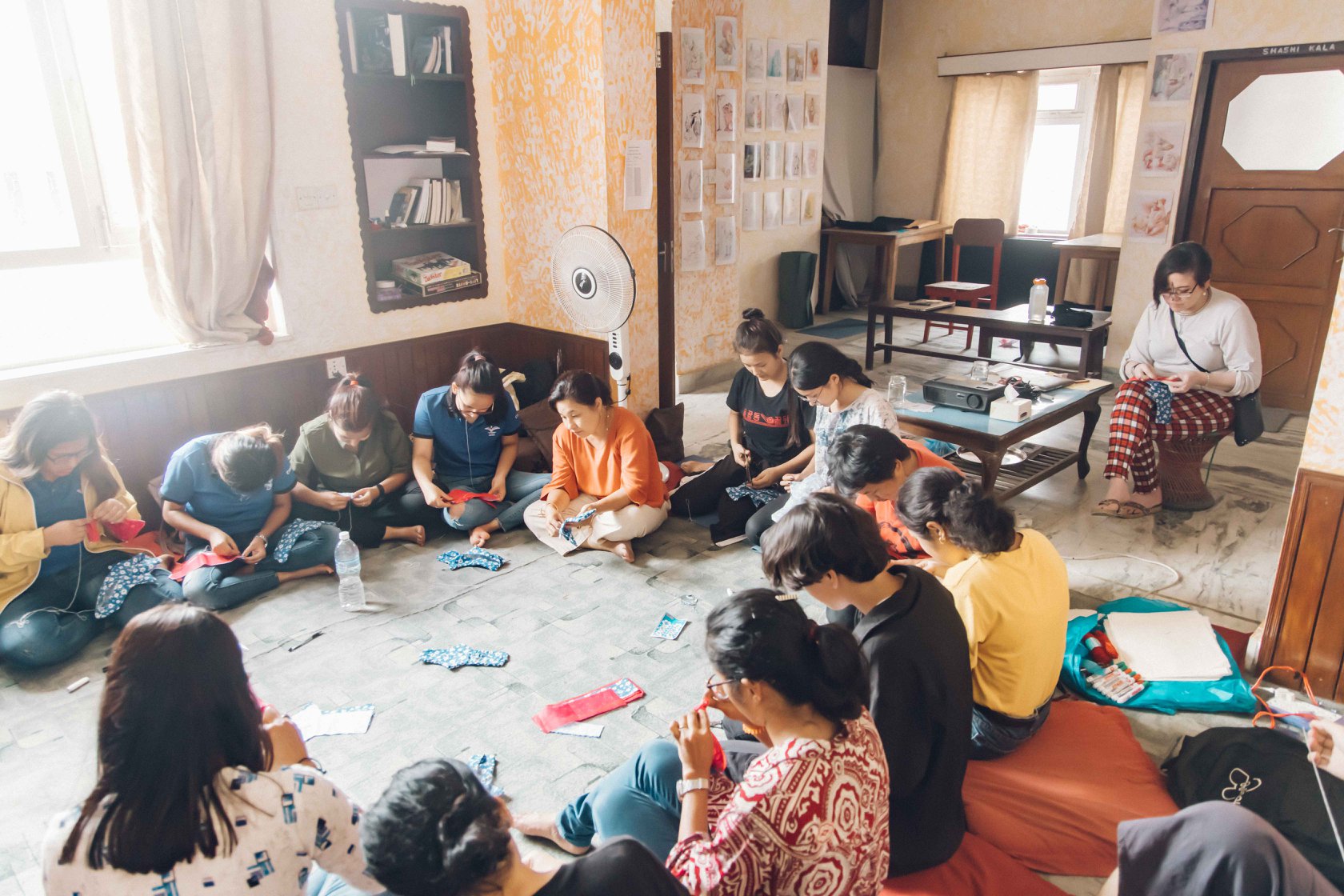 Workshop participants sewing and talking in a circle on the floor